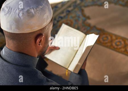 Over the shoulder view of a young Muslim man reading the Quran Stock Photo