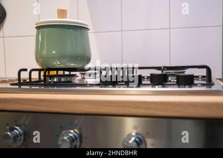 a light green saucepan with a lid stands on a home gas stove, home cooking, home kitchen interior Stock Photo