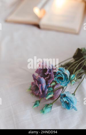 Bouquet of flowers and a book on white bed sheets. Stock Photo