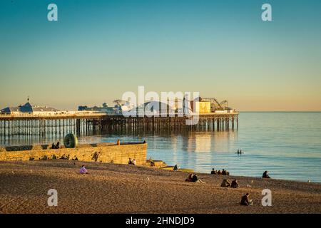 13 January 2022: Brighton, East Sussex, UK - People sitting on Brighton Beach at sunset on a clear winter evening, near the Doughnut Groyne and... Stock Photo