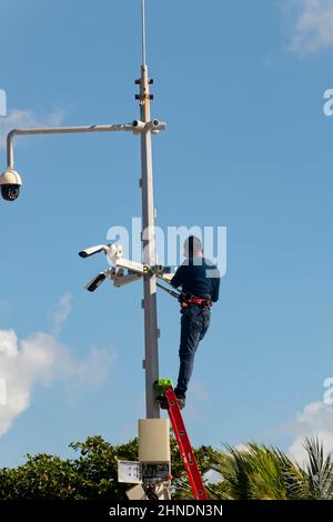 A man on a metal ladder installs security cameras near a public beach in Mexico Stock Photo