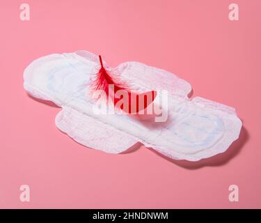 Sanitary napkin pad with red elegant feather lying on pink background Stock Photo
