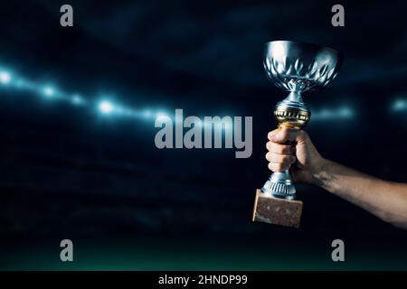 winner hand holding up a trophy cup on stadium background. copy space
