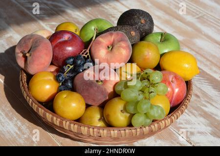 Basket of organic fruit, including grapes, plums, nectarines,  flat peaches, lemon, apples and avocados Stock Photo