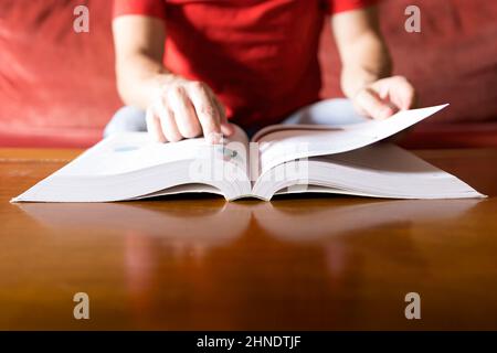 A person in a red shirt consults the solution in a book and finds it, blurred background, selective focus Stock Photo