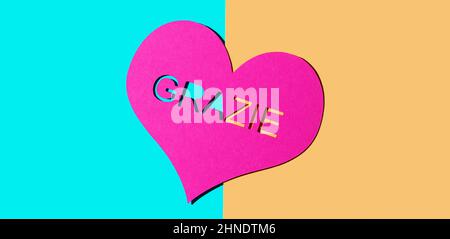 a pink heart with the text thank you written in italian, on a blue and orange background, in a panoramic format to use as web banner or header Stock Photo