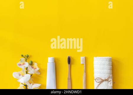 Natural eco-friendly bamboo brushes, white towel, tube of toothpaste and orchid flower. Set for washing on paper yellow background. Copy space for tex Stock Photo