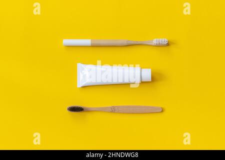Two natural eco-friendly bamboo brushes with white and black bristles and tube of toothpaste. Set for washing on yellow paper background. Copy space f Stock Photo