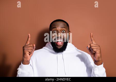 Photo of impressed funny guy dressed white sweatshirt pointing fingers up empty space isolated brown color background Stock Photo