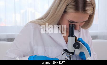 Female laboratory assistant analyzes samples using a microscope while working at a table in a laboratory, doing research Stock Photo