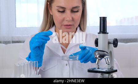 female research chemist scientist in a medical suit and protective gloves conducts research on samples with a micropipette and test tubes for working Stock Photo