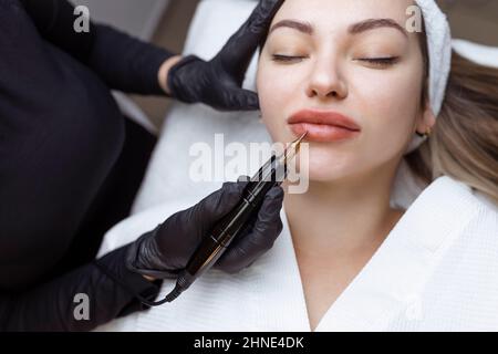 Cosmetologist makes permanent makeup on a woman's face. Specialist applies a tattoo on the patient's lips close-up Stock Photo