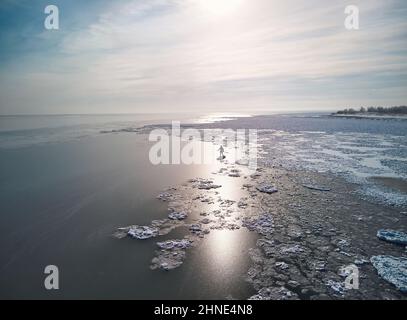 Man athlete is paddling on sup board in the lake with ice at winter time. Aerial Drone shot. Extreme outdoor sport concept Stock Photo