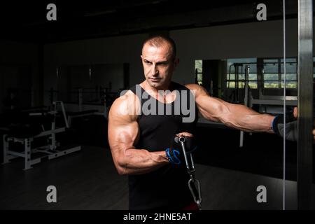 Man In The Gym Exercising On His Biceps On Machine With Cable In The Gym Stock Photo