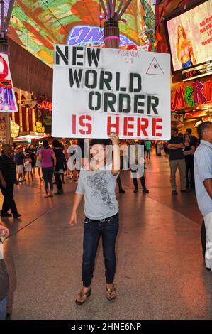 A young female protester on Fremont Strret in Las Vegas holds a large white sign with black and red letters that reads “New World Order is here.” Stock Photo