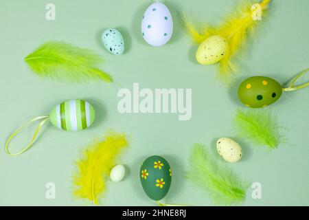 Beautiful festive Easter frame made of colored eggs, feathers on a green background. Copy space for your design. View from above. Place for text. Stock Photo