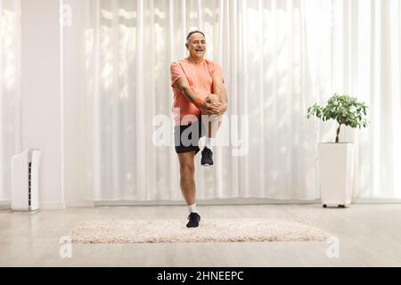 Mature man in sportswear stretching his leg and smiling at home Stock Photo