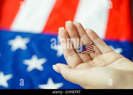 Close up of young woman holding United State of America pin in her hand. American flag on the background. USA Patriotism concept. Stock Photo