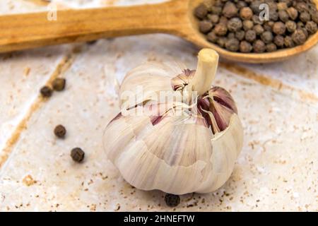 head of garlic on tile floor with peppercorns in a wooden spoon Stock Photo