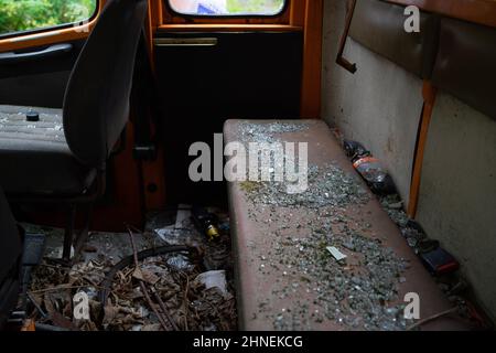 Broken glass on a rear bench seat of an old orange delivery van in front of an old abandoned sanatorium, Germany Stock Photo