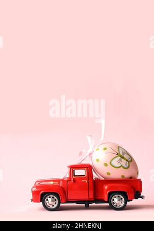One Easter egg on a small car on a pink background. Copy space. Easter card. Stock Photo