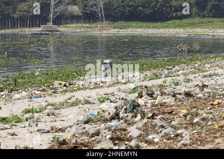 A man collects discarded plastic items on the banks of the river Buriganga, in Dhaka, Bangladesh, February 16, 2022. Industrial waste and sewage from the city are all dumped into the rivers. The once fresh and flowing rivers like Buriganga, is now submerged in pollution. The other rivers of the country face the same fate. Recent research has brought an even more horrendous picture into view. And that is plastic pollution. In just the four rivers that surround the capital city Dhaka, 30,000 tonnes of plastic waste were discovered. Half of this was in the river Buriganga. (Photo by Suvra Kanti D Stock Photo