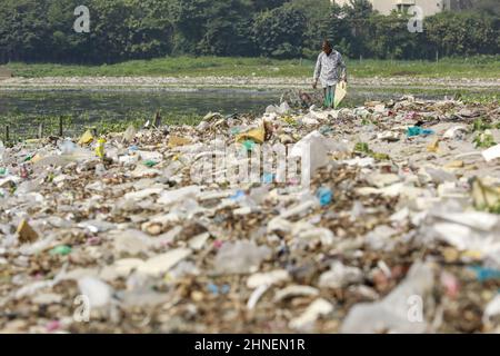 A man collects discarded plastic items on the banks of the river Buriganga, in Dhaka, Bangladesh, February 16, 2022. Industrial waste and sewage from the city are all dumped into the rivers. The once fresh and flowing rivers like Buriganga, is now submerged in pollution. The other rivers of the country face the same fate. Recent research has brought an even more horrendous picture into view. And that is plastic pollution. In just the four rivers that surround the capital city Dhaka, 30,000 tonnes of plastic waste were discovered. Half of this was in the river Buriganga. (Photo by Suvra Kanti D Stock Photo