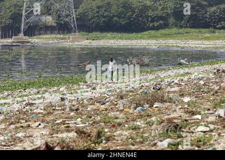 A man collects discarded plastic items on the banks of the river Buriganga, in Dhaka, Bangladesh, February 16, 2022. Industrial waste and sewage from the city are all dumped into the rivers. The once fresh and flowing rivers like Buriganga, is now submerged in pollution. The other rivers of the country face the same fate. Recent research has brought an even more horrendous picture into view. And that is plastic pollution. In just the four rivers that surround the capital city Dhaka, 30,000 tonnes of plastic waste were discovered. Half of this was in the river Buriganga. (Photo by Suvra Kanti D Stock Photo