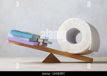 Roll of toilet paper outweighed money on scales, bloated economy concept, money is paper Stock Photo