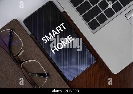 Top view of phone on table near laptop, notepad and glasses with inscription smart home. Stock Photo