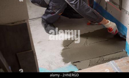 Applying tile adhesive to the floor. Spreading wet mortar before applying tiles on bathroom floor. puts adhesive. Stock Photo