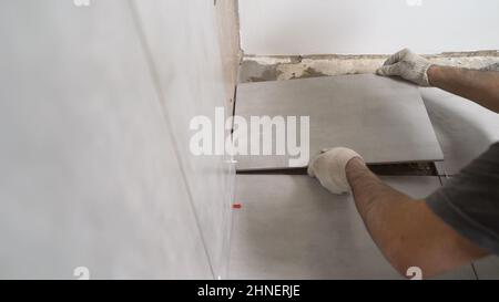 The craftsman glues the tiles to the bathroom wall. The master tiler glues the gray ceramic wall tiles. Stock Photo