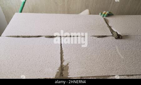 A worker erects a wall from a block. Bricklayer builder working with autoclaved aerated concrete blocks. Engineering and constructions concepts. Stock Photo
