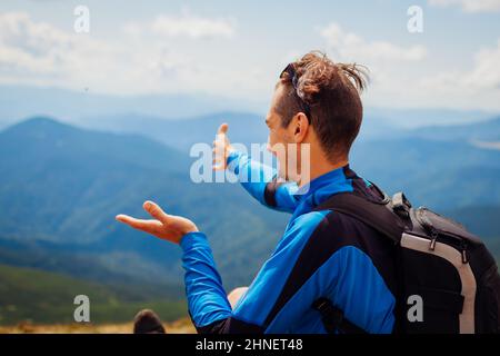 Trip to Carpathian mountains. Happy man hiker with backpack pointing on view on top of Hoverla enjoying landscape. Traveling in summer Ukraine Stock Photo