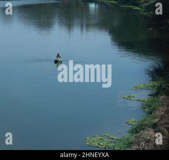 Lone fisherman on a rubber tube casting his net in calm river waters. Location: Nashik, Maharashtra, India.  Date: February 16 2022 Stock Photo