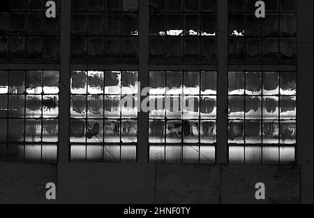 Large Partially Blacked out Windows of an Old Warehouse with Sun Shining Partially Through. Black and White Stock Photo