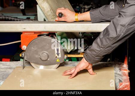 A worker cuts porcelain tiles on an industrial tile cutter with a diamond blade. Stock Photo