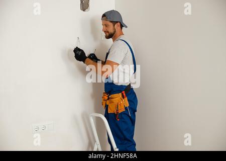 Busy handyman electrician holding screwdriver while working on residential electric system Stock Photo