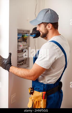 Electrical technician in uniform looking focused while checking fuses in a switchboard Stock Photo