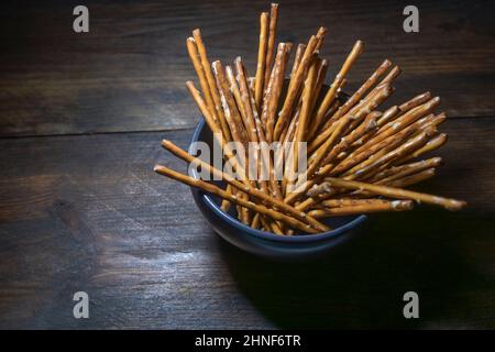 Salty pretzel sticks in a bowl on a dark rustic wooden table, crunchy snack food often served in the evening in pubs or at home while watching TV, cop Stock Photo