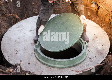 The plumber covers the sewer well with a manhole cover. Water supply and sewerage in a residential building. Stock Photo