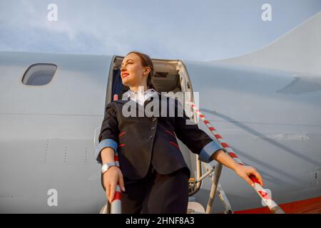 Joyful woman stewardess standing on airplane stairs Stock Photo