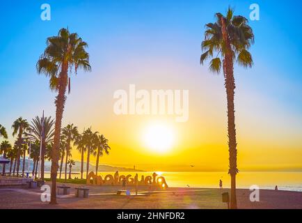 MALAGA, SPAIN - SEPTEMBER 29, 2019:  The scenic palm trees and bright sunrise over Malagueta beach with a view of its sign silhouette in front of the Stock Photo