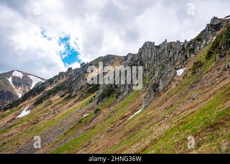 Rock cliff covered with moss over steep slope and hill against cloudy sky Stock Photo