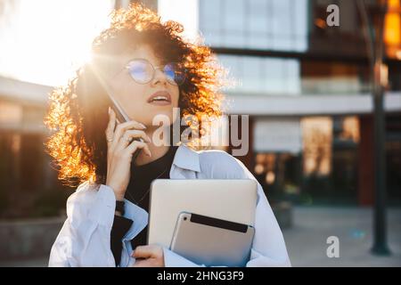 Successful caucasian woman entrepreneur with curly hair using mobile to make a phone call. Beautiful portrait Stock Photo