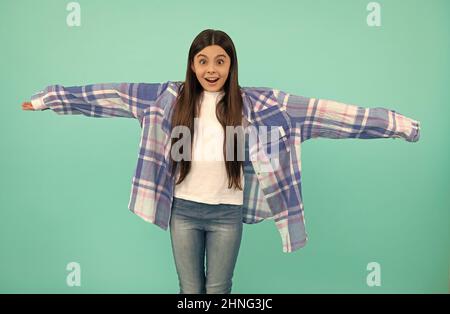 Surprised kid try on oversized plaid shirt with extra long sleeves blue background, fashion Stock Photo