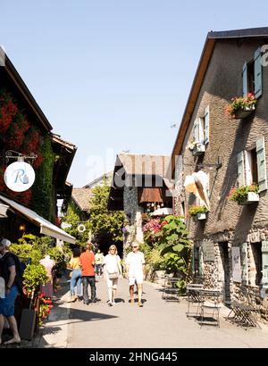 Tourists walk past the shops and restaurants of the Grande Rue on a summer day in the medieval town of Yvoire, France. Stock Photo