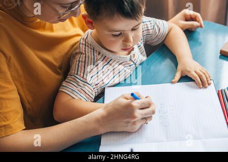 Top view of woman helping adorable son doing schoolwork at home, solving math exercise. Education, learning, study. Quarantine lifestyle. Quarantine Stock Photo