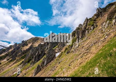 Rock cliff covered with moss over steep slope against cloudy sky Stock Photo
