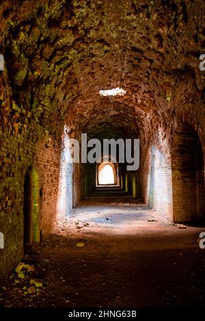 Sunlight shines through hole from brick ceiling in passage of old abandoned fort Stock Photo